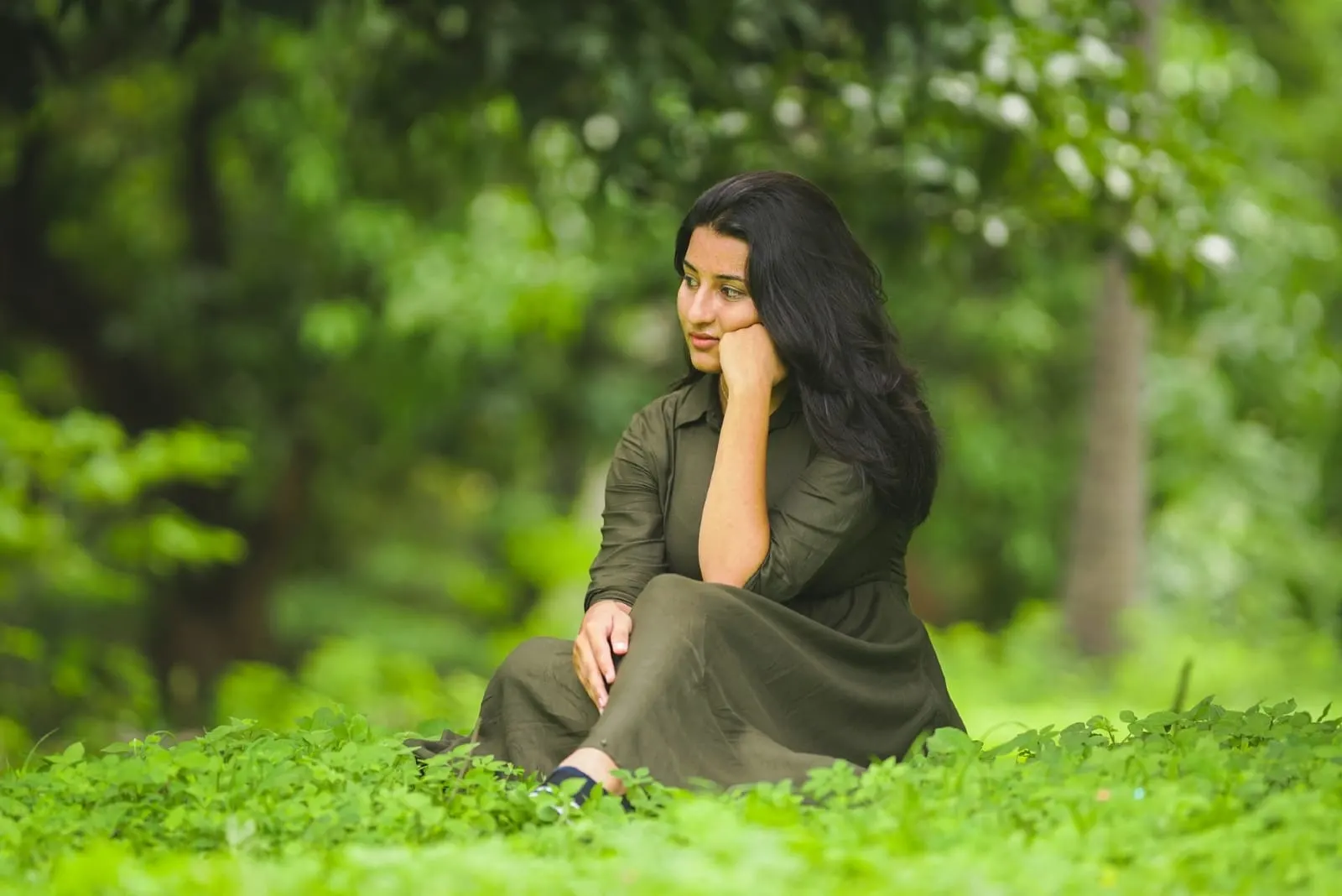 pensive woman in green dress sitting on grass
