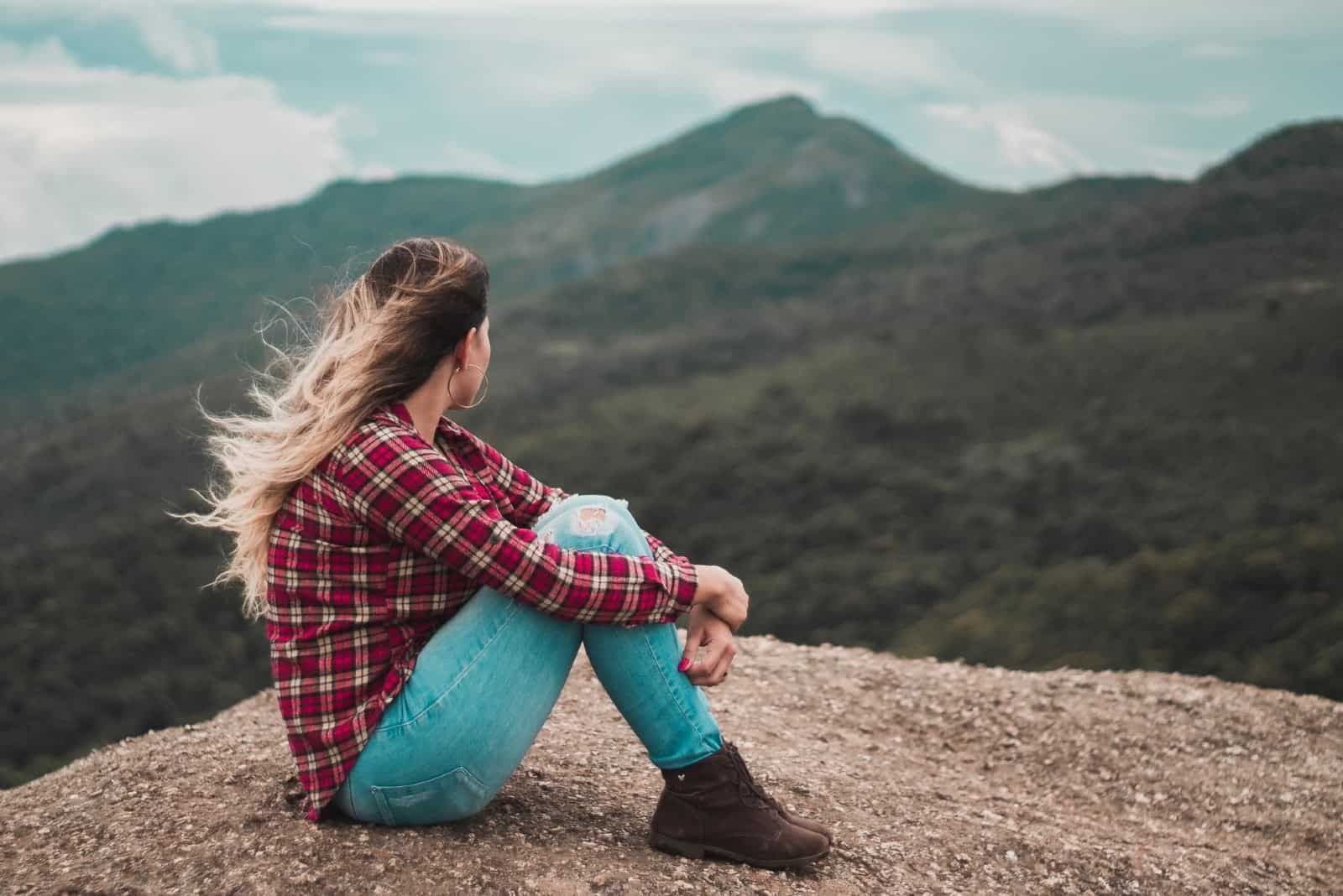 mujer sentada en el suelo mirando la montaña