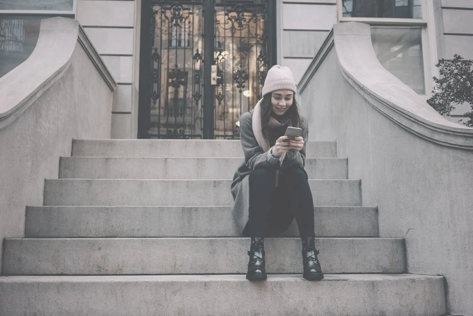 woman sitting on the stairs outside a building and texting on phone