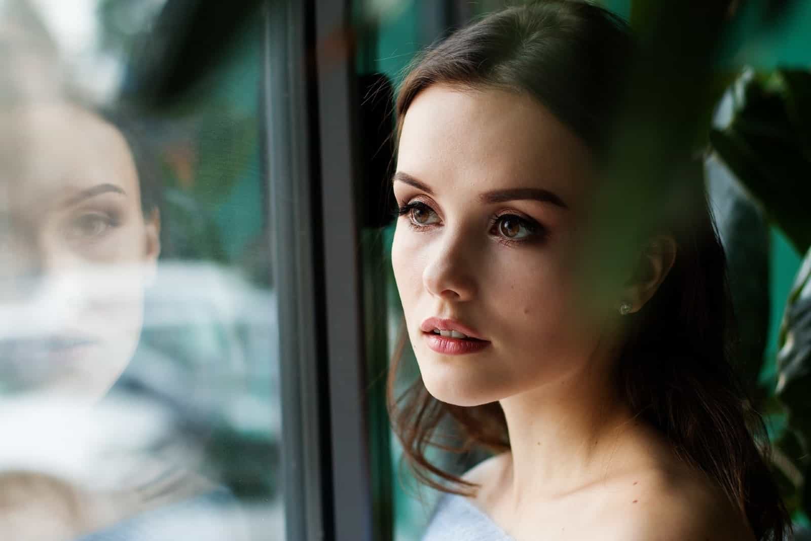 pensive woman standing near window during daytime