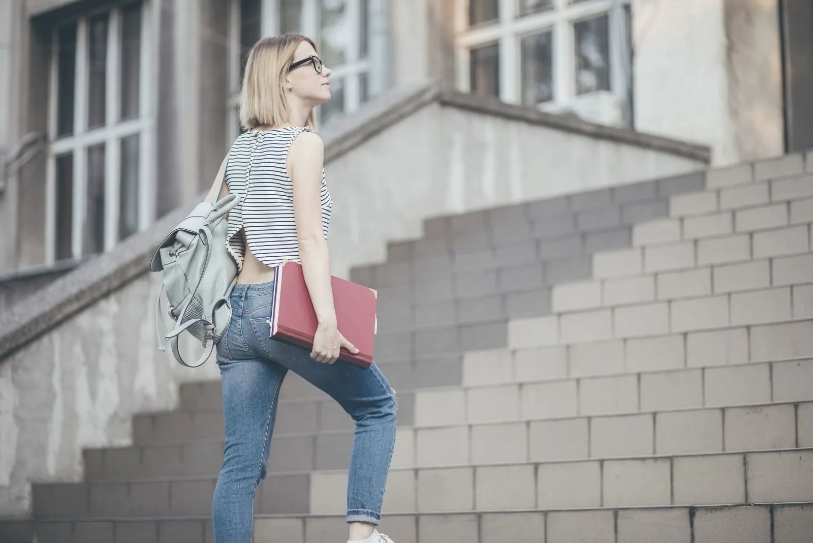 woman student climbing the stairs carrying books and looking hopeful