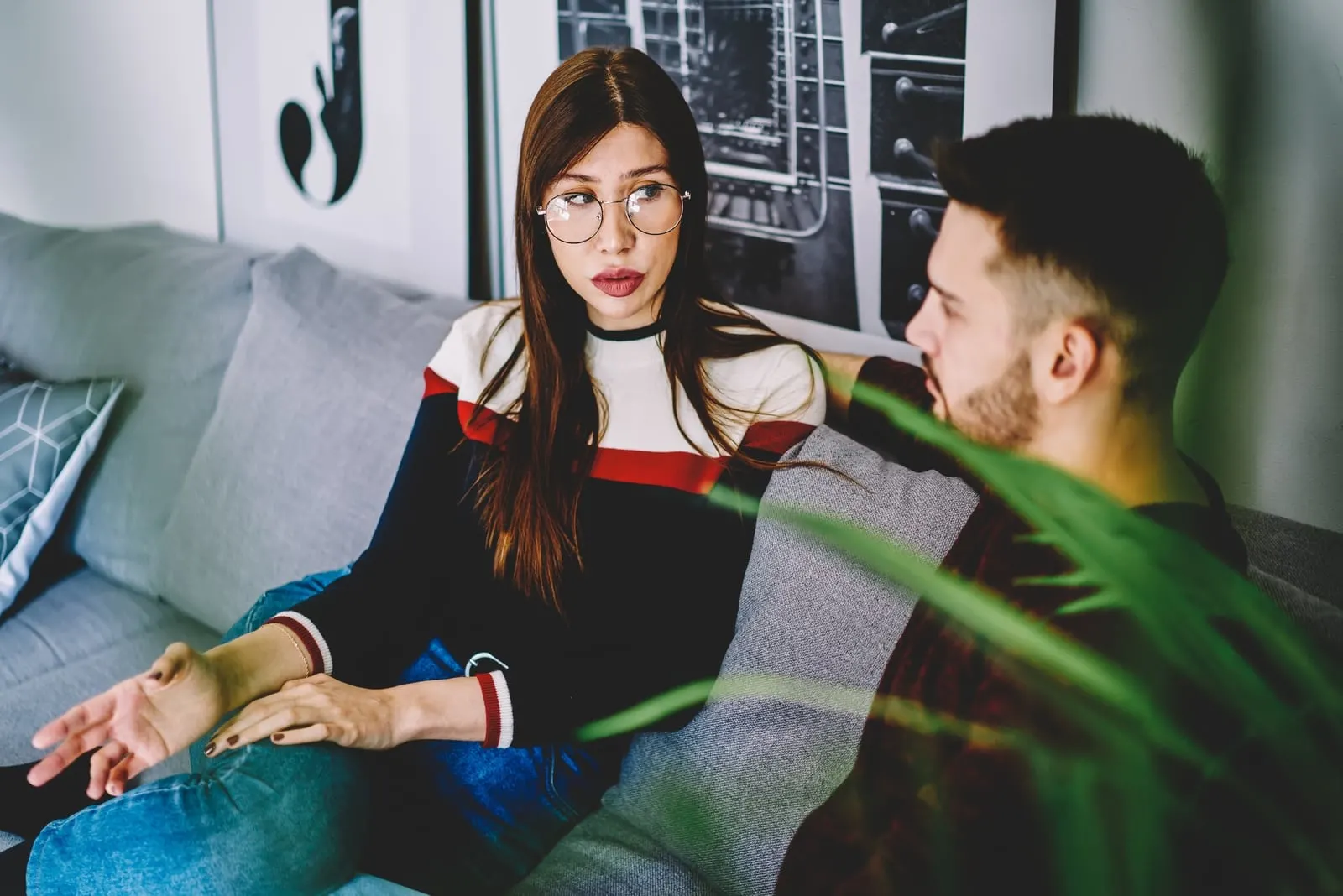 woman with eyeglasses talking to man while sitting on sofa