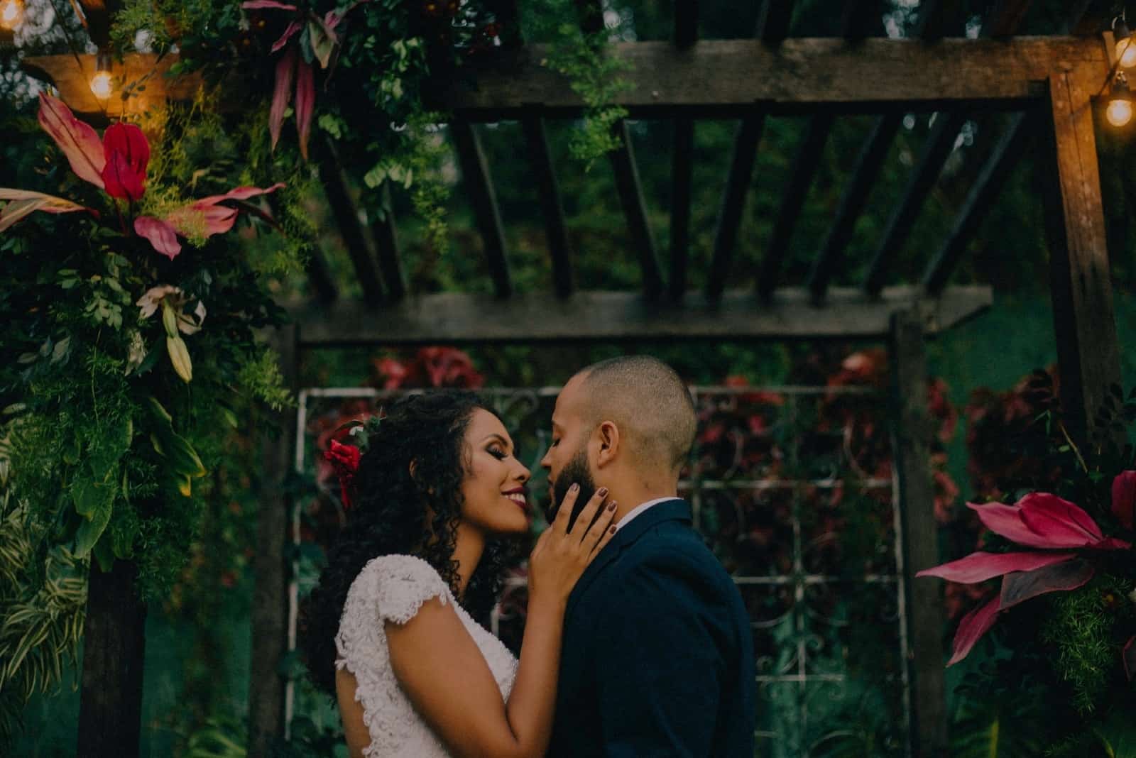 bride touching groom's face while standing near plants