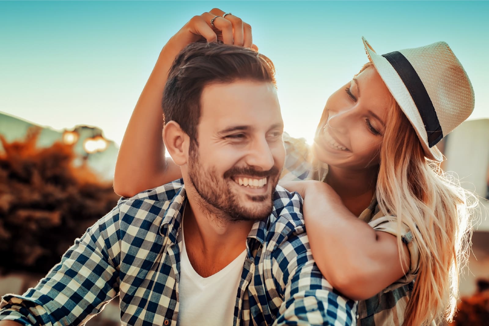 mujer feliz con sombrero tocando el pelo de un hombre al aire libre