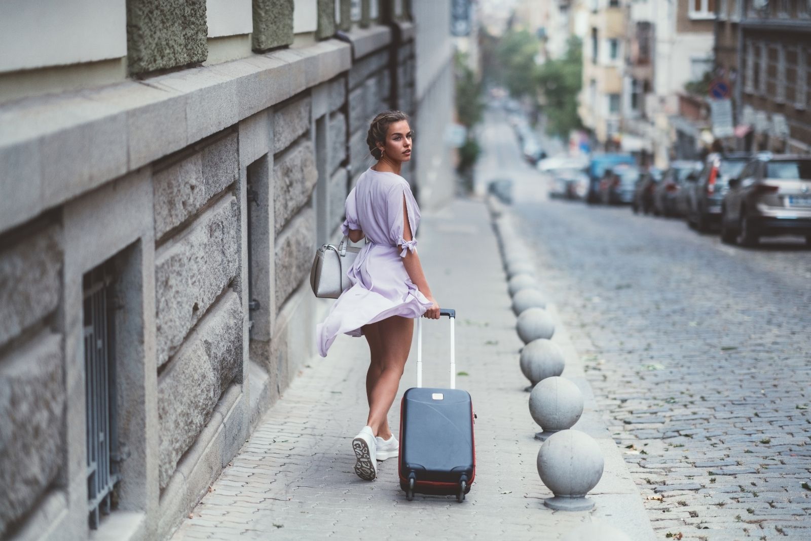 mujer viajando sola mirando hacia atrás llevando equipaje por el paseo lateral 