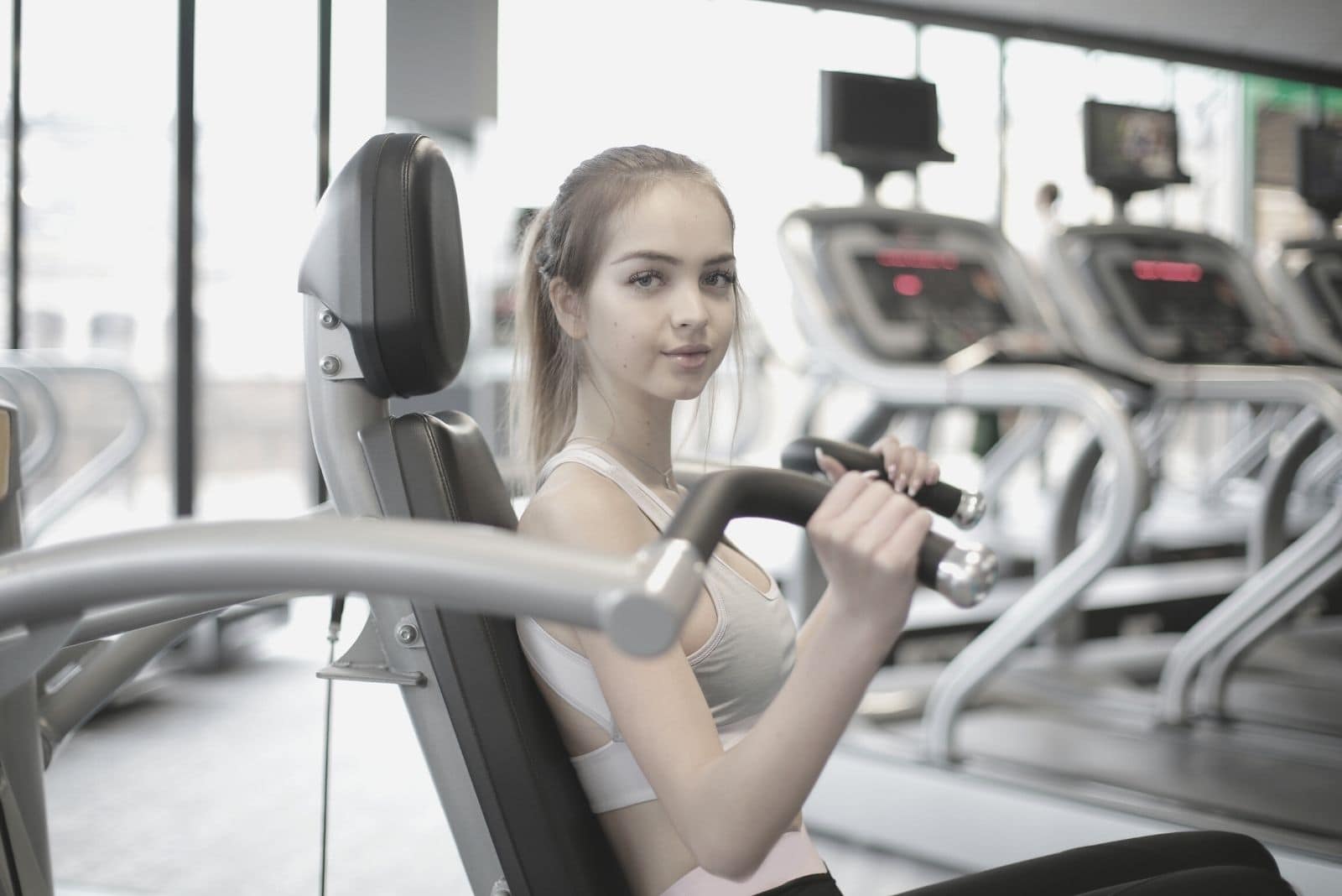 mulher a usar um equipamento para fazer exercício no ginásio, olhando para a câmara