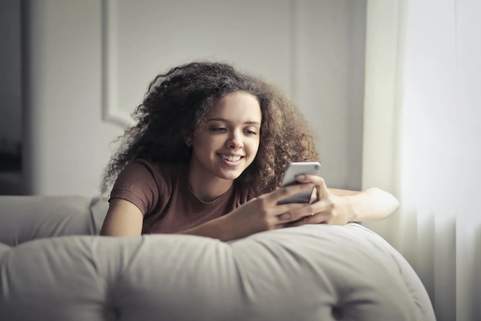 happy woman using smartphone while sitting on sofa