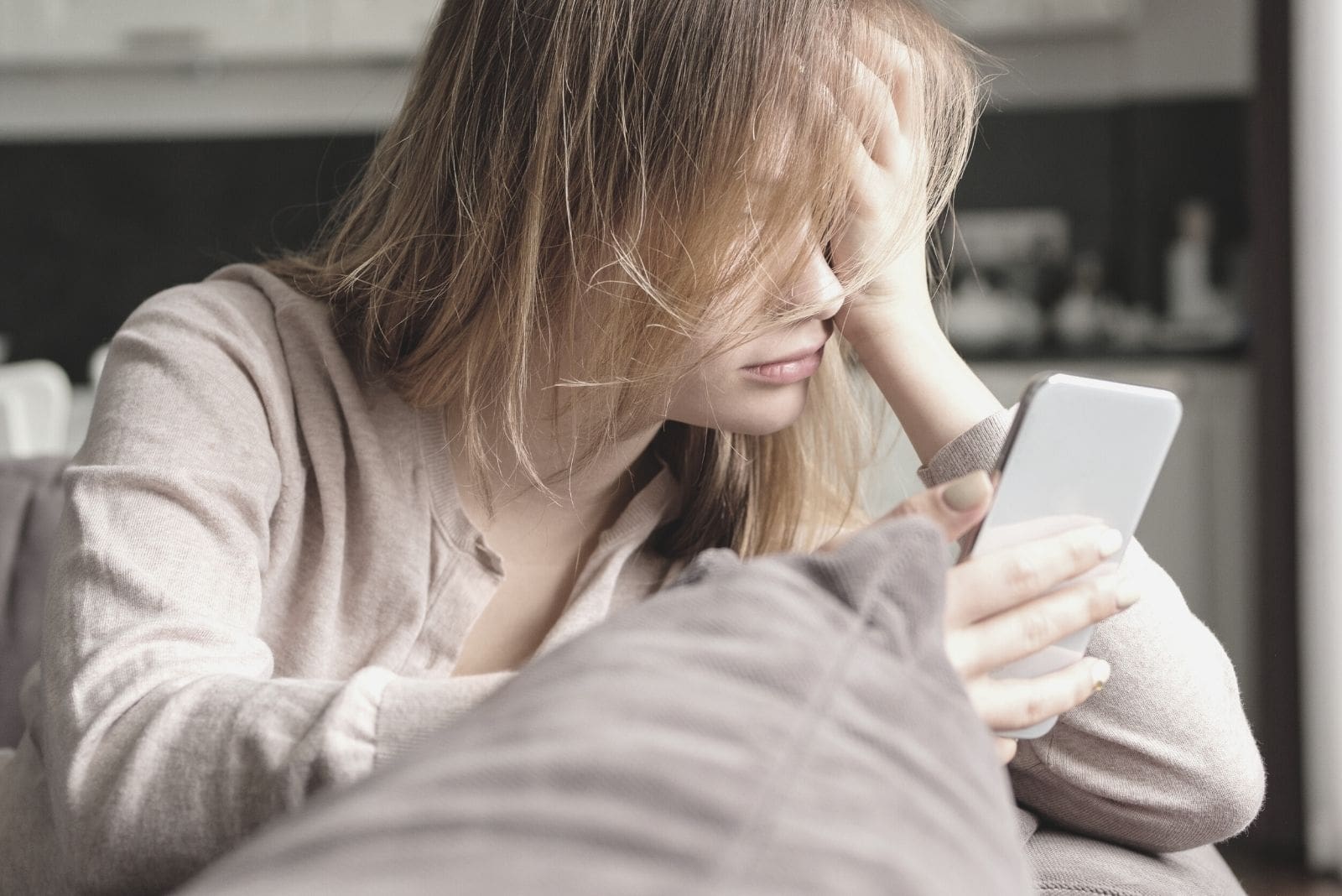 mulher com cabelo desarrumado a olhar para o seu smartphone enquanto se apoia no sofá 