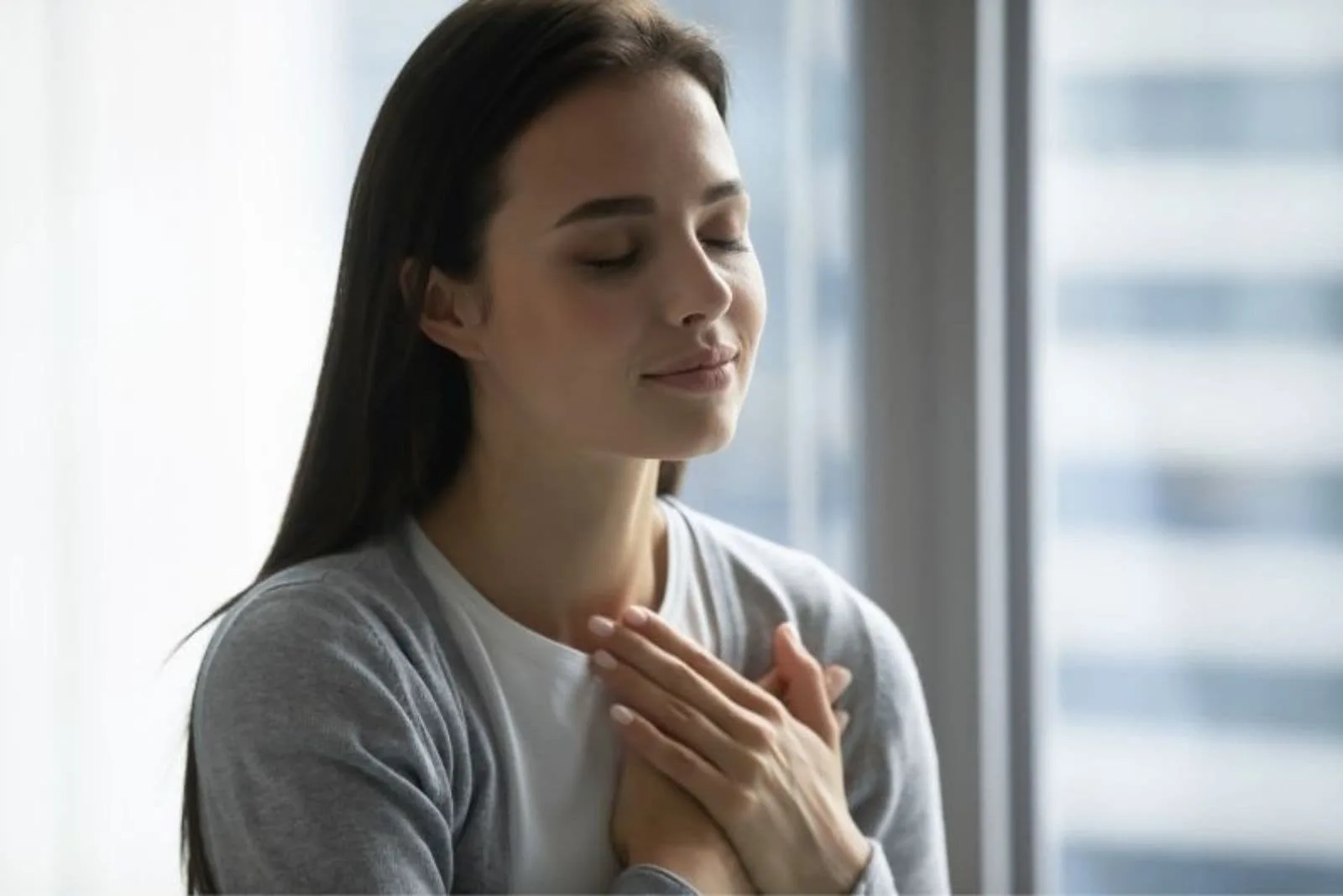 womans closing eyes with hands on chest standing inside 