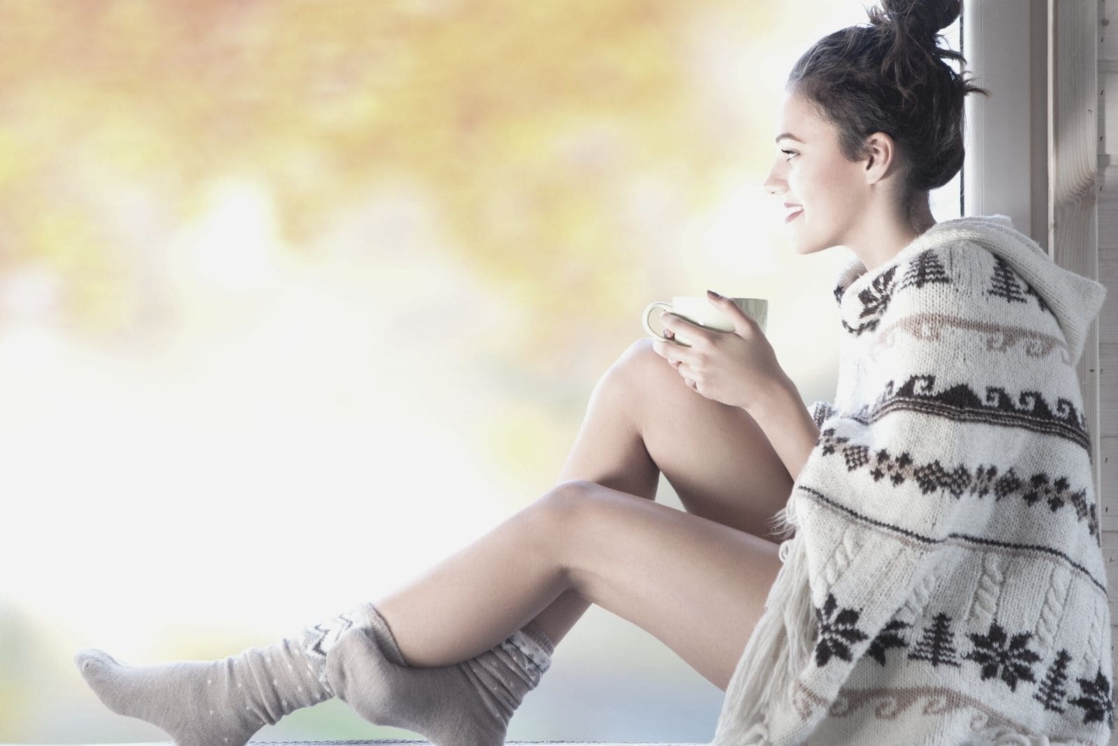 young beautiful brunette smiling while sipping the morning coffee sitting on the ledge