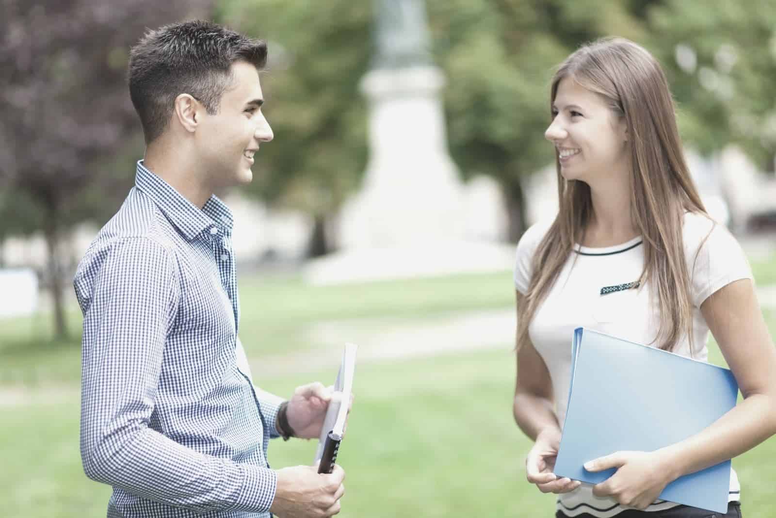 joven pareja hablando al aire libre de pie en el campo de la escuela