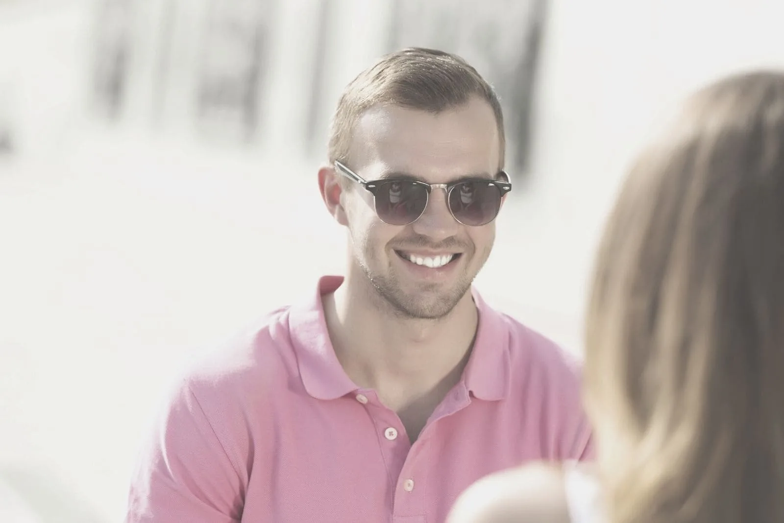 young man in pink top wearing sunglasses smiling at a woman outdoors