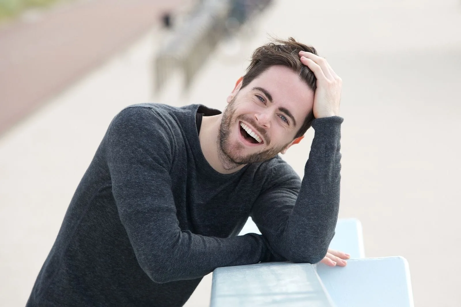 young man laughing holding his head leaning on the ledge outdoors