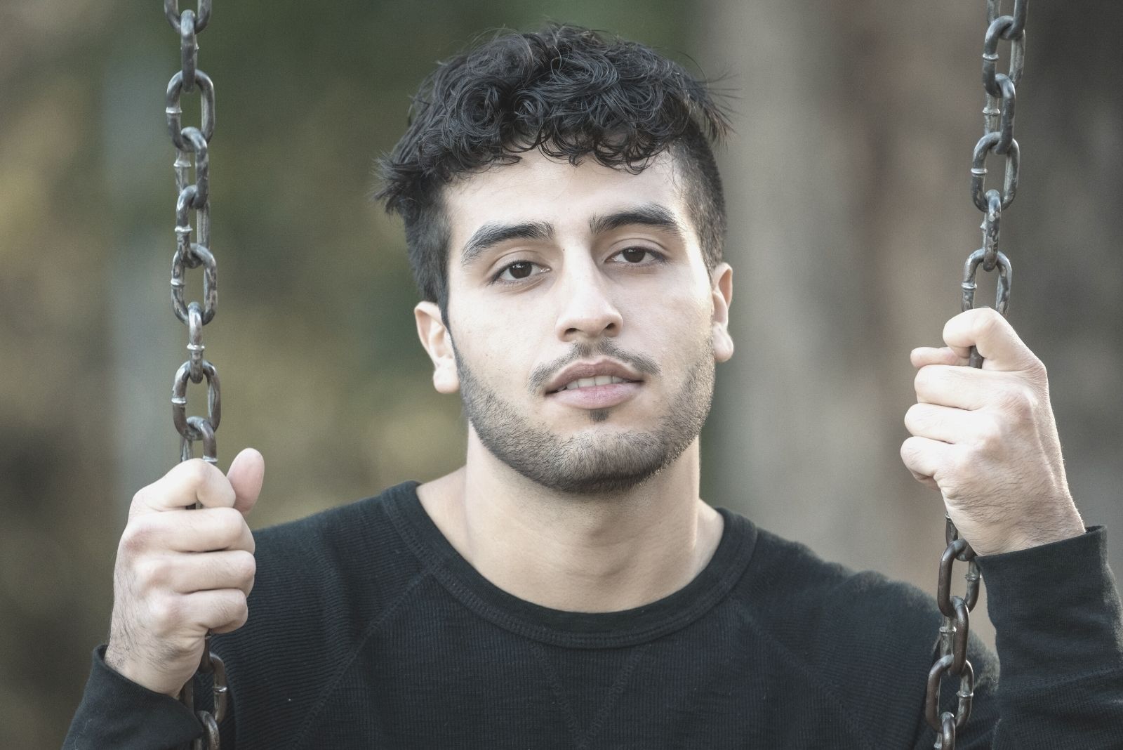 young man looking at the camera smiling sitting on the swing of the park in close up image