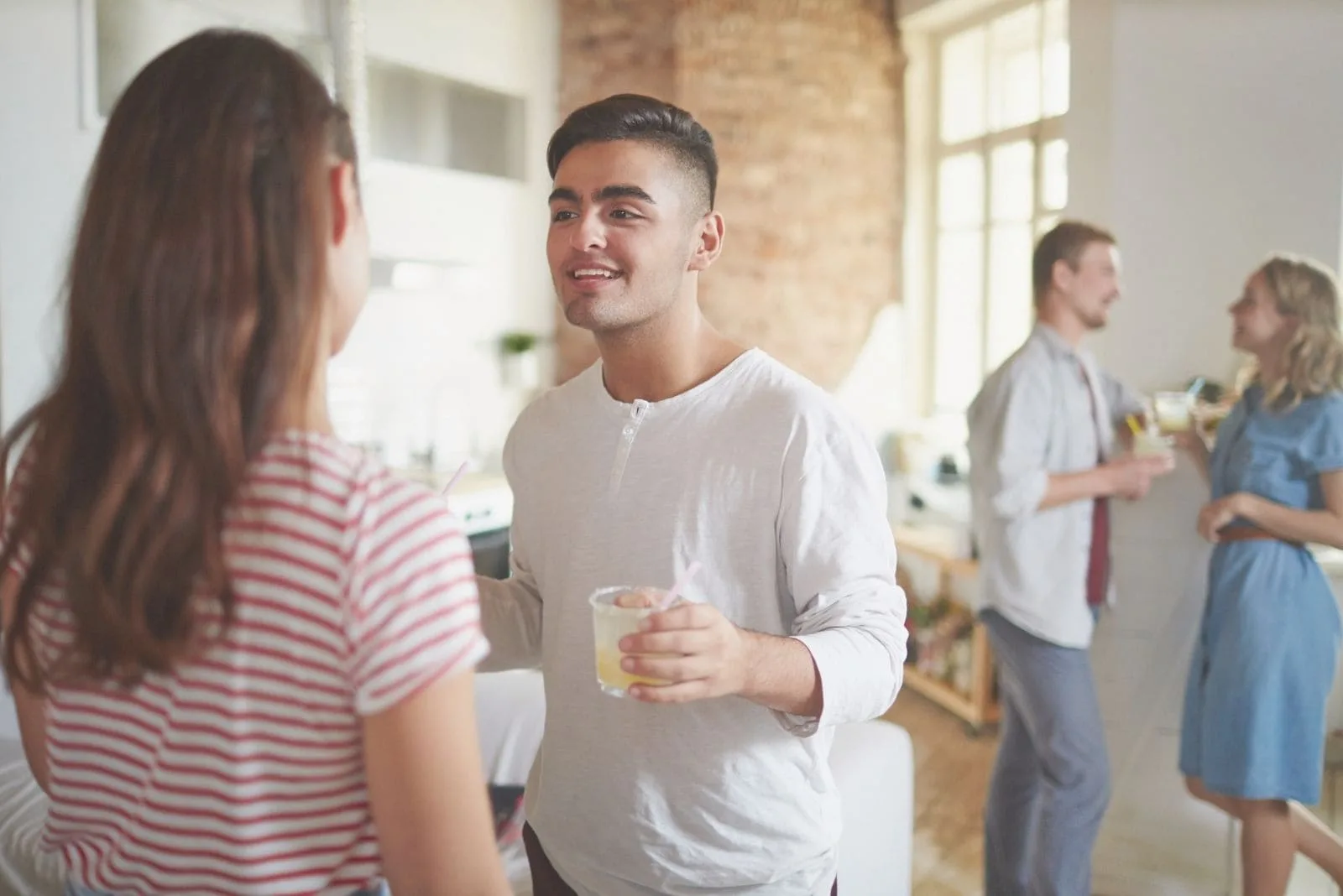 young man with drink talking to his girlfriend with another couple standing and talking at the background