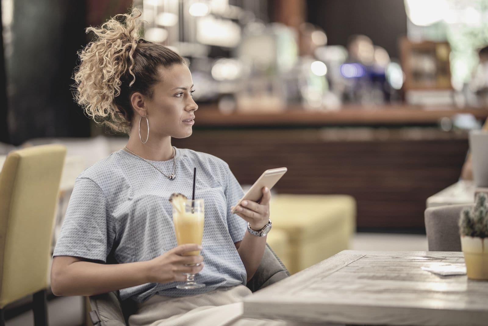 giovane donna pensierosa seduta al bar e con il telefono in mano mentre guarda altrove