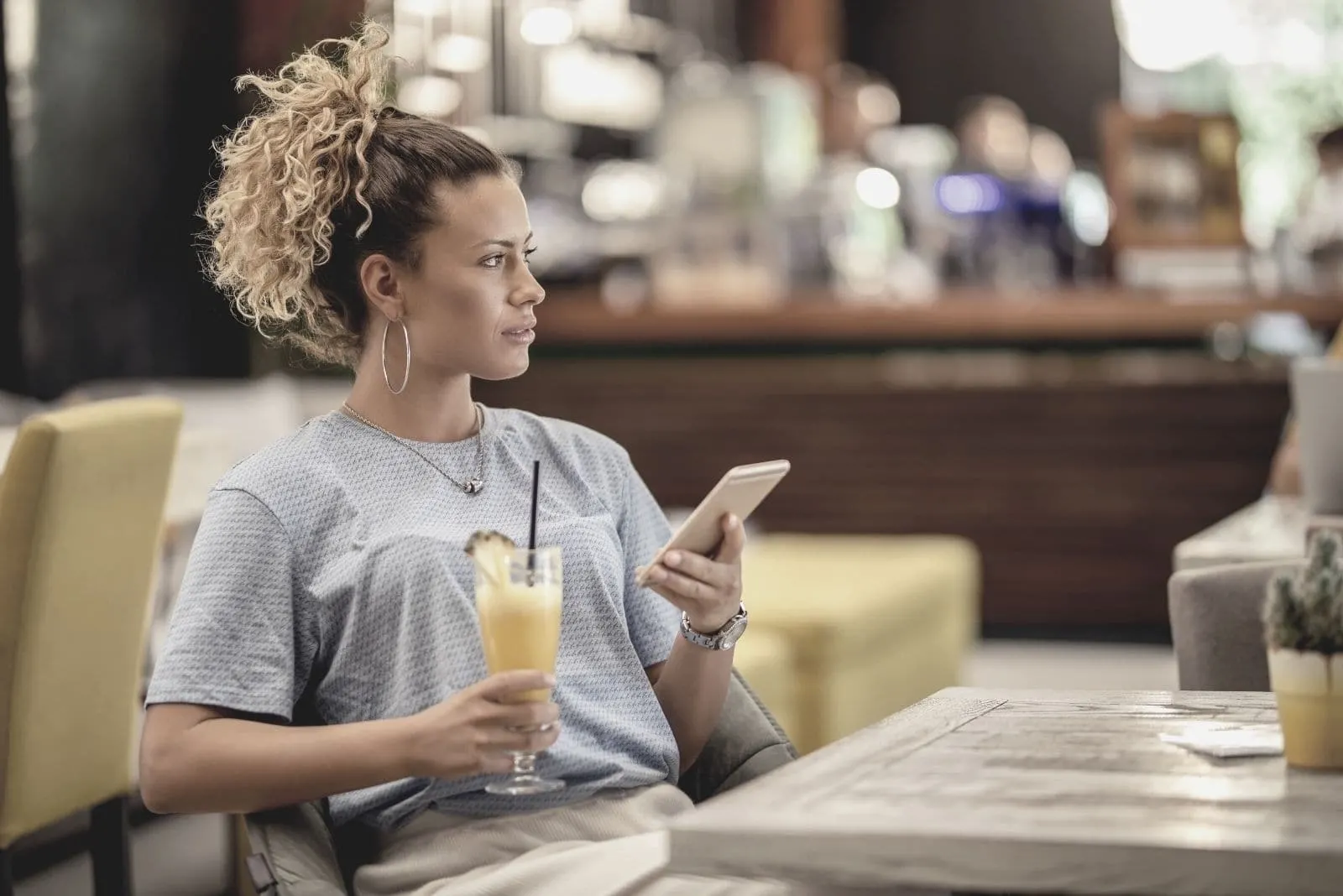 young pensive woman sitting in the bar and holding a phone while looking away