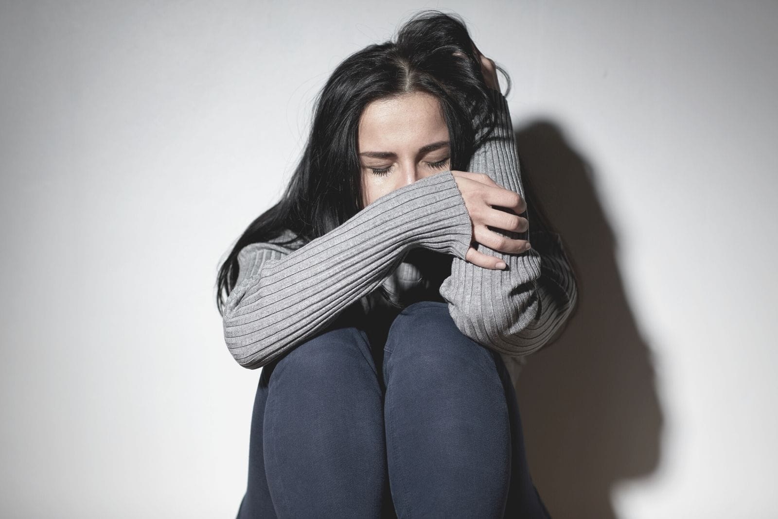 young woman crying tucking in sitting on the floor and leaning on the wall of the room