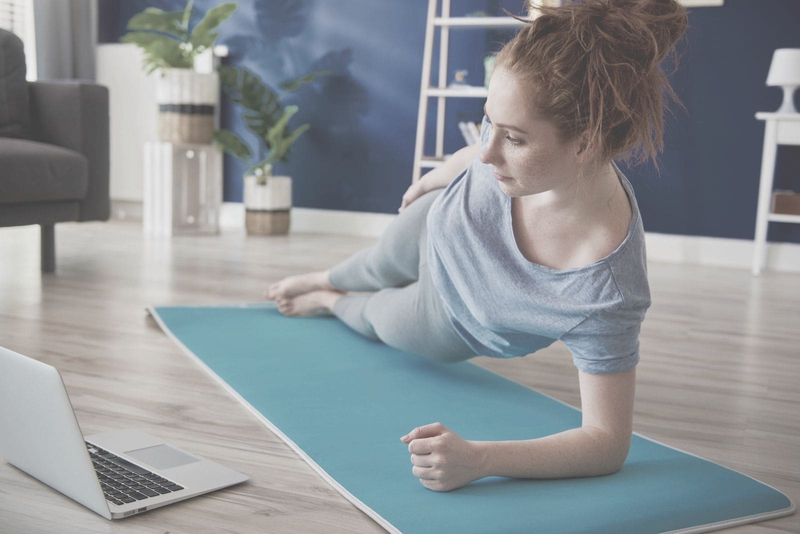 young woman exercising on mat while watching video on laptop at home