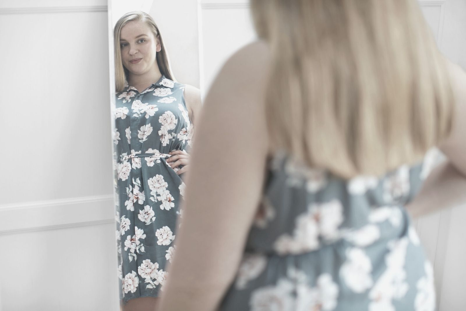 mujer joven mirando su cuerpo sonriendo al espejo con vestido floral