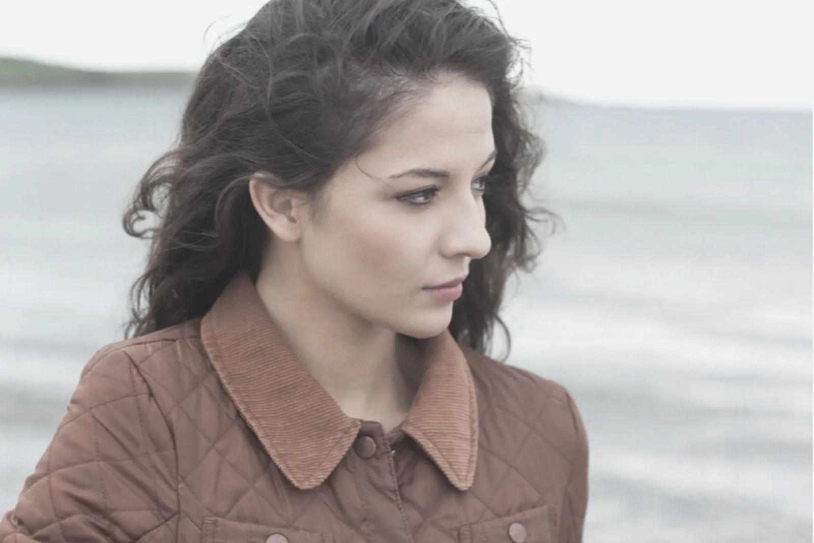 young woman thoughtful and looking at the sea wearing coat in close up image