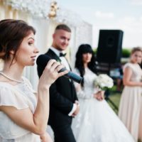 woman talking on microphone while standing near groom and bride
