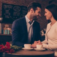 man and woman holding hands while sitting in cafe