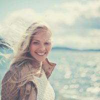mulher bonita a sorrir e a caminhar na praia, olhando para a câmara