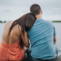 woman leaning on man's shoulder while sitting on dock