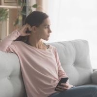 mujer esperando y sentada en el sofá sosteniendo un smartphone en casa