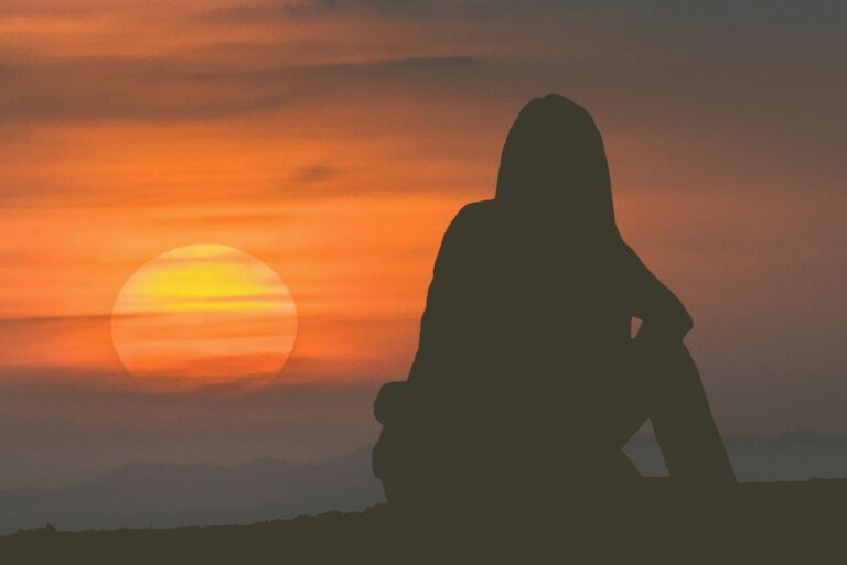 backview of a woman watching the sunset alone sitting near the body of water