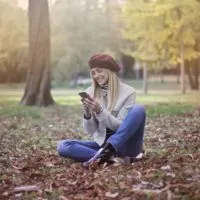 blonde woman using smartphone while sitting on ground