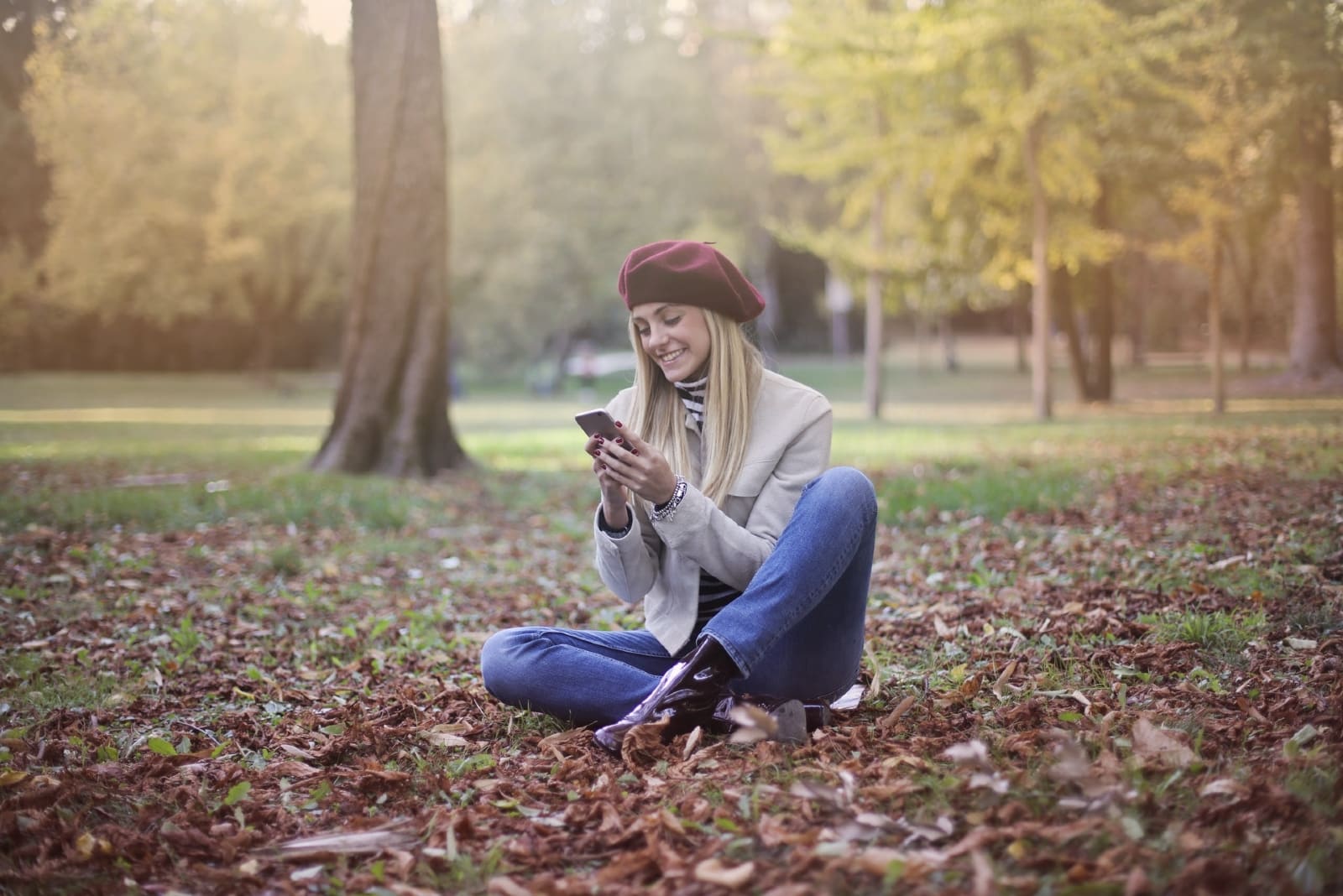 blonde woman using smartphone while sitting on ground