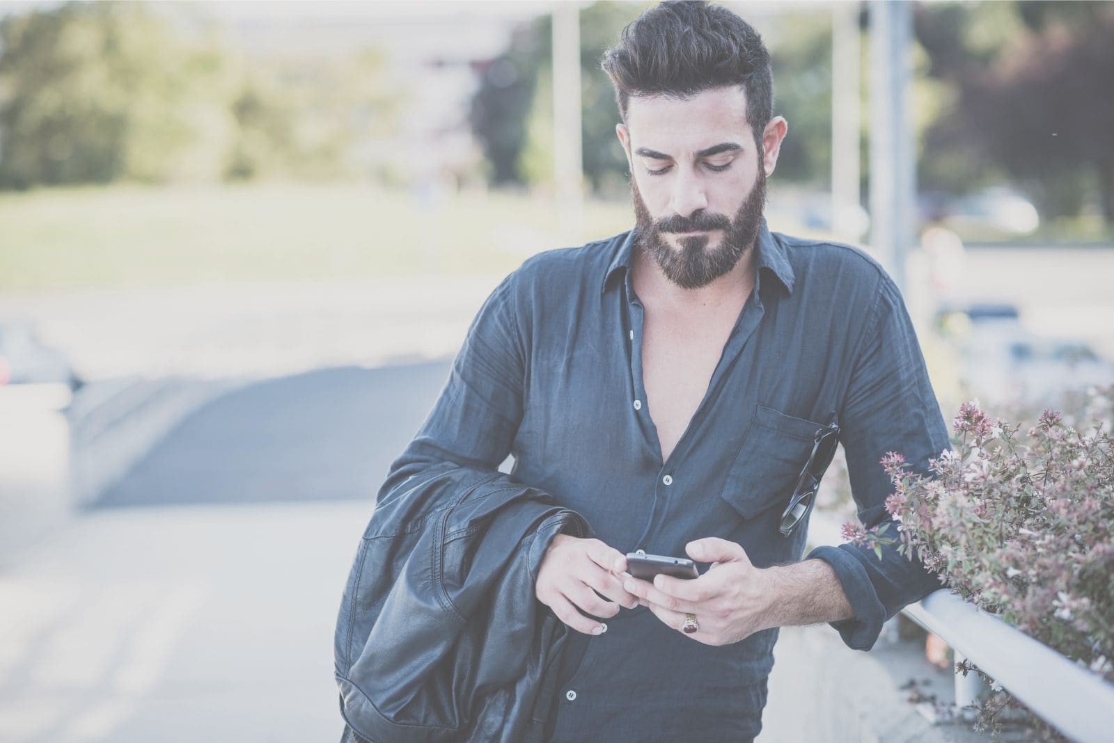fashionable man standing and leaning while looking at his cellphone by the streetside