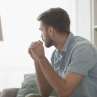 homem triste sentado no sofá da sala de estar a olhar para as janelas