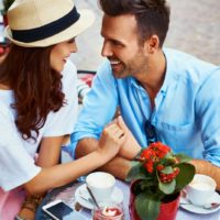 hombre y mujer tomados de la mano sentados en cafe al aire libre