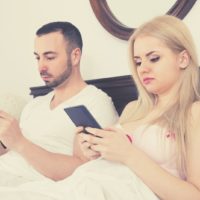 phubbing couple silent busy with their smartphone while sitting in bed