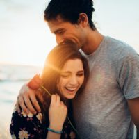 a man hugs a smiling woman holding a rose in her hand