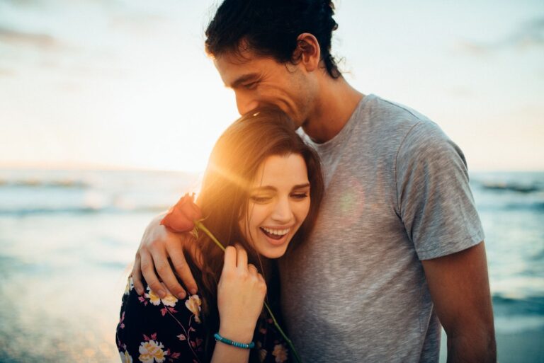 a man hugs a smiling woman holding a rose in her hand