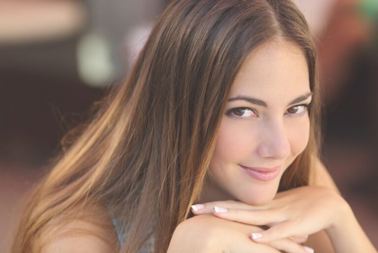 young pretty woman with smooth skin and hair leaning on her hand and looking at the camera