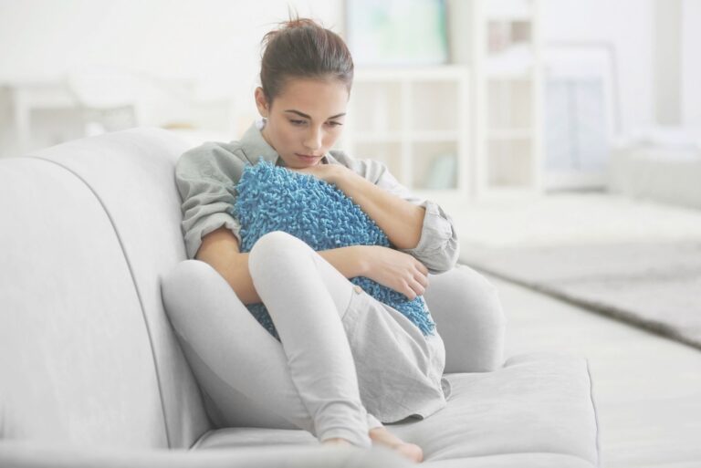 sad pensive woman embracing a pillow lounging in the sofa inside the livingroom