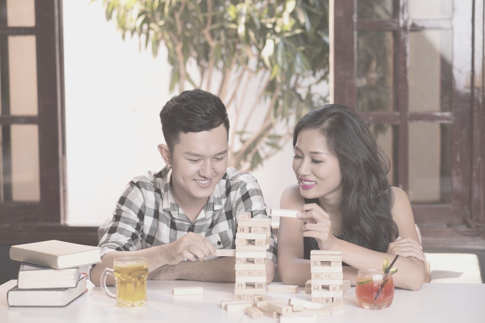 asian couple playing jenga game indoors with drinks on the side