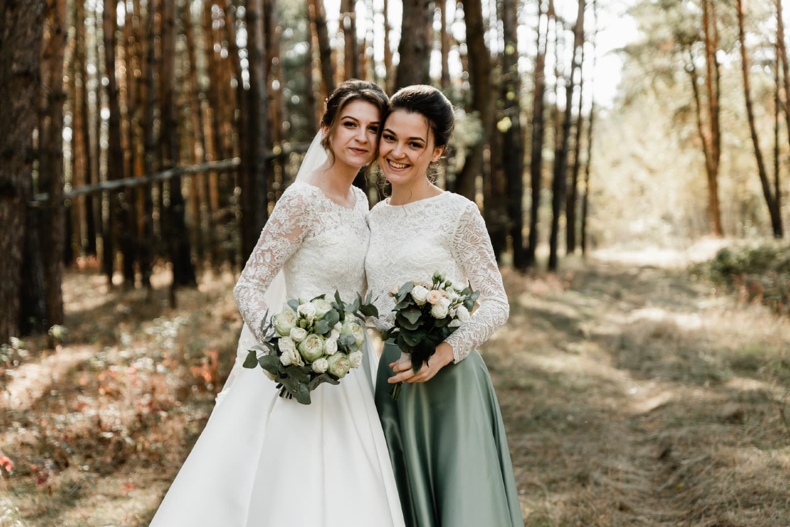 bride and bridesmaid with bouquet of flowers standing in forest