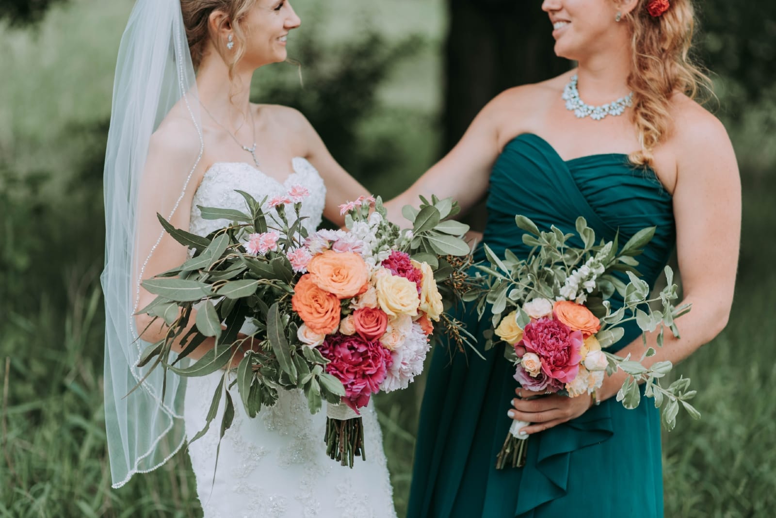 bride and bridesmaid standing outdoor holding bouquet of flowers