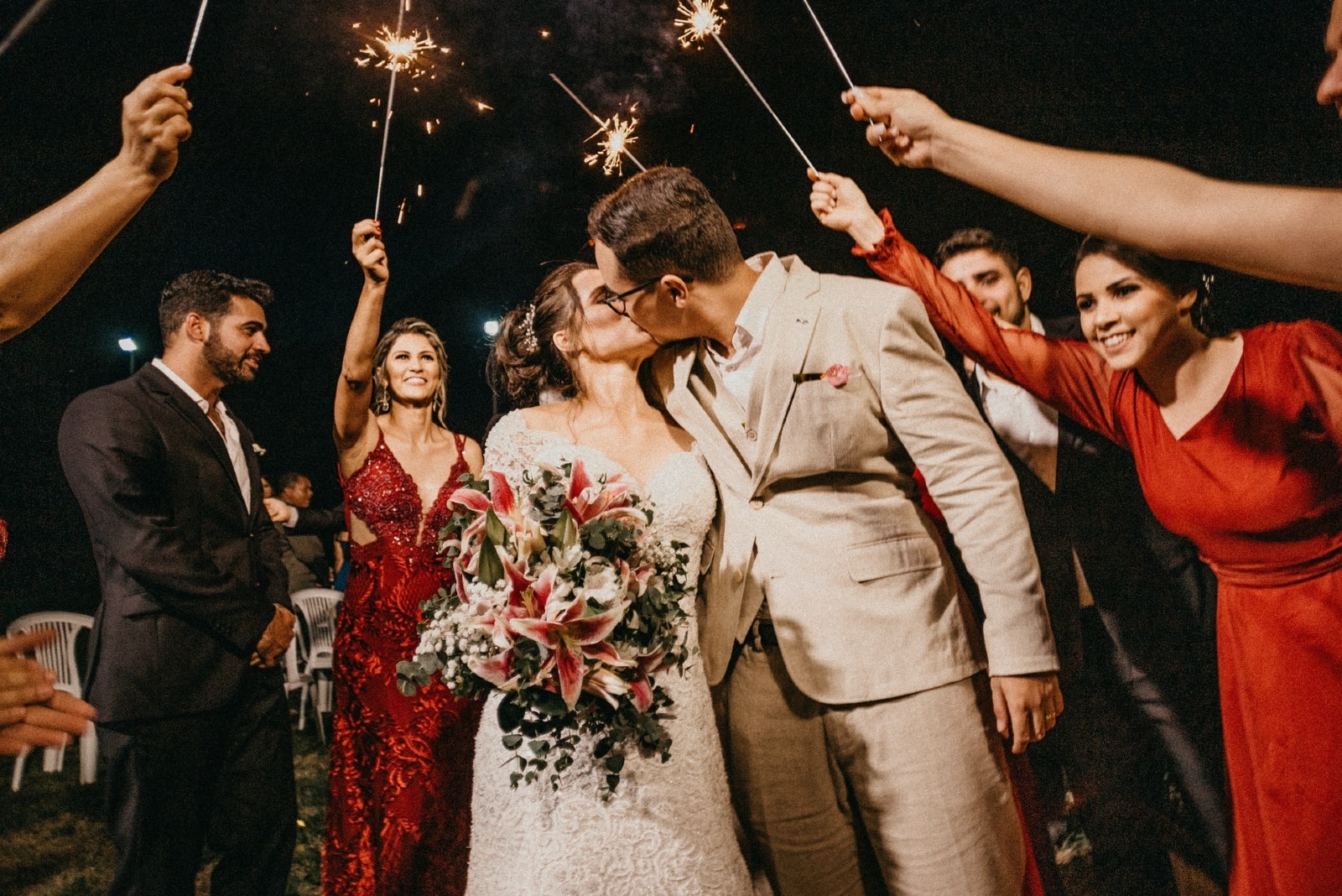 bride and groom kissing while people holding sparkles