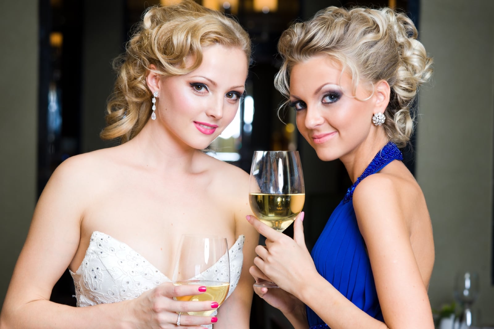 bridesmaid in blue dress and bride holding glasses of wine