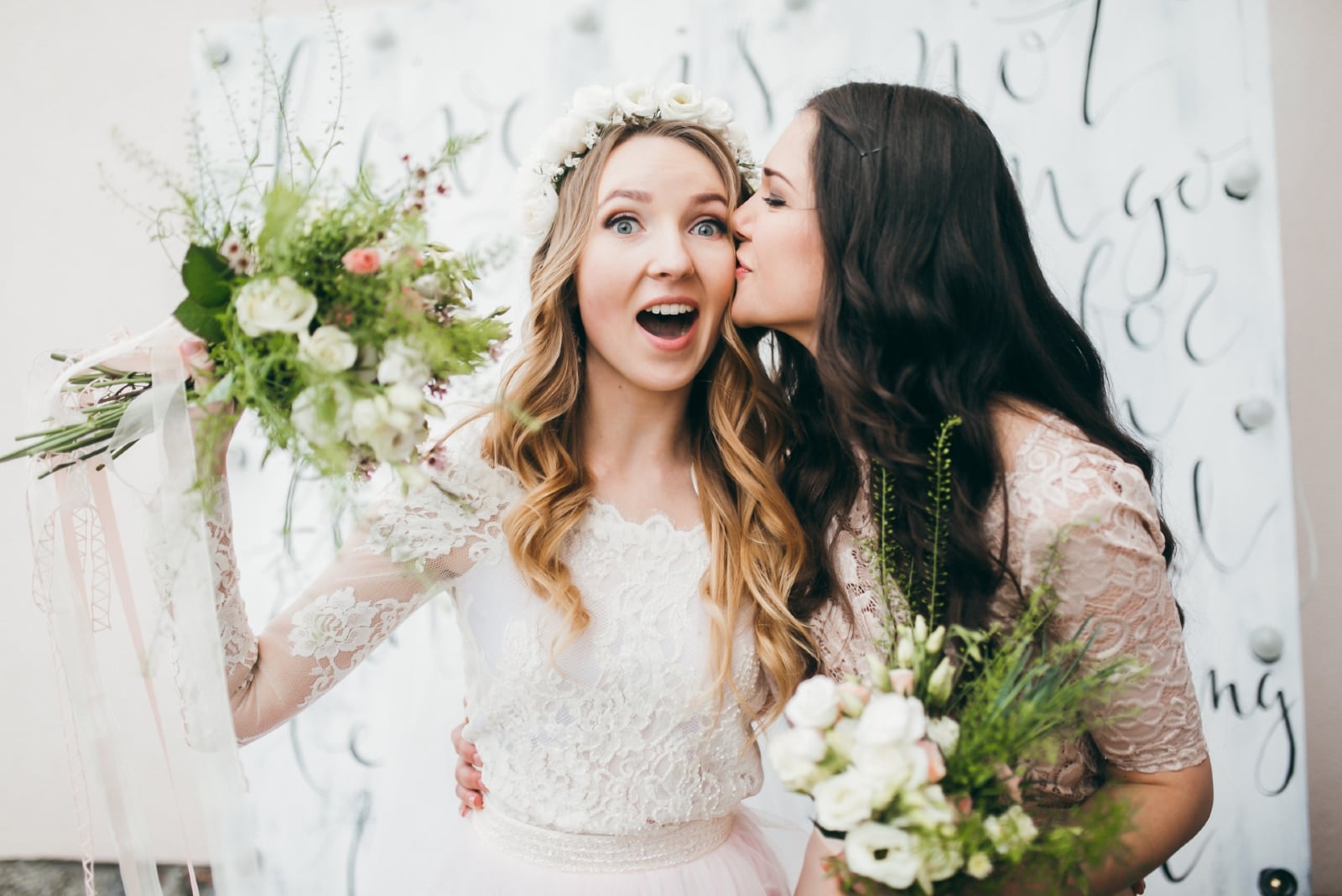 bridesmaid kissing bride on cheek while holding bouquet of flowers