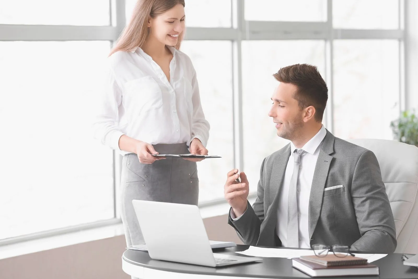 colleagues working in office with the woman standing near the man sitting by his office table