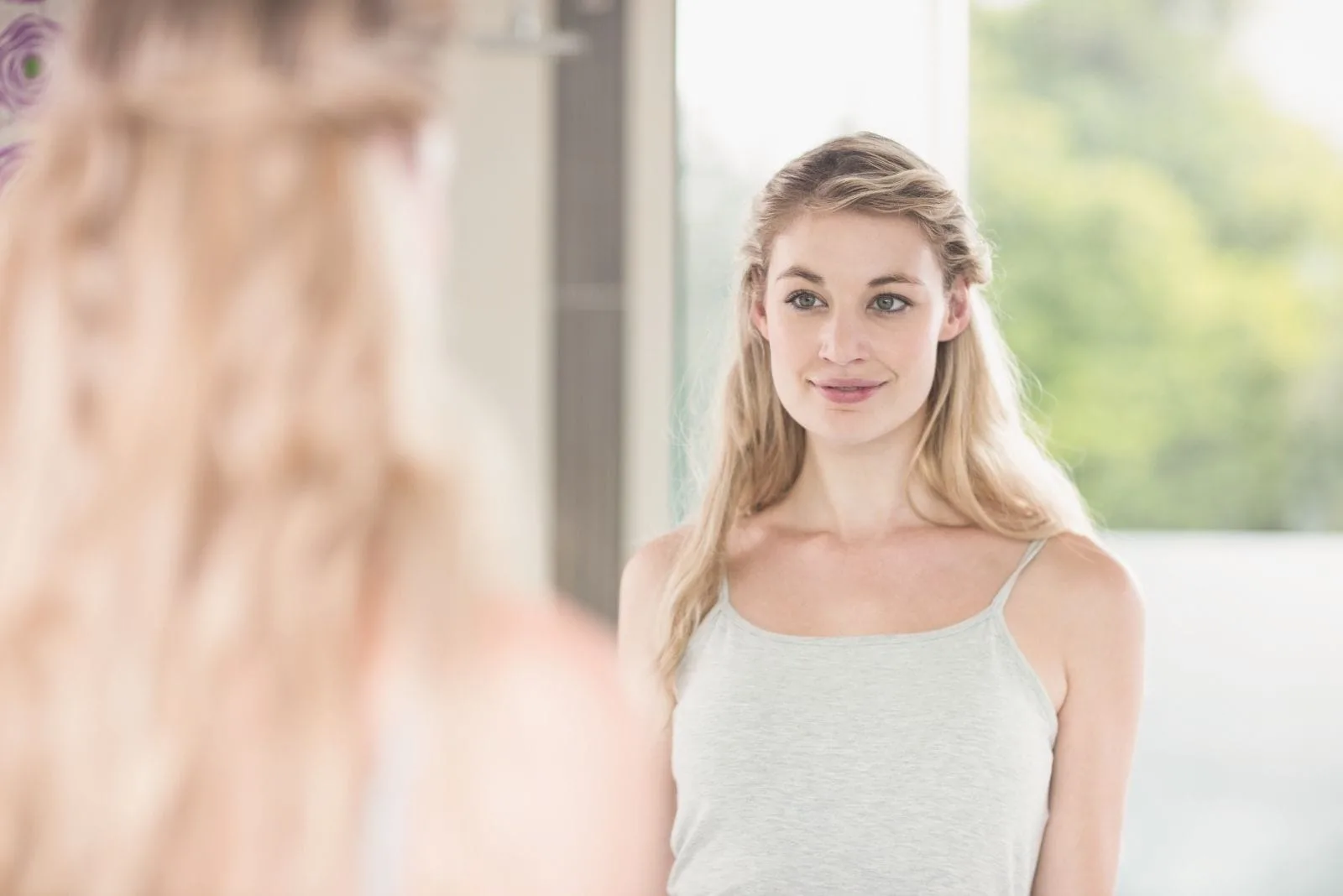 confident young blonde woman looking at herself at the mirror