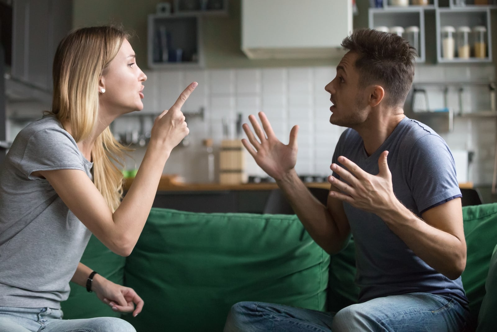 man and woman arguing while sitting on green sofa